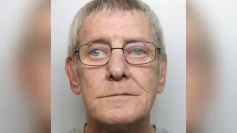 Staffordshire Police A mugshot of an elderly man with short grey hair and glasses. He is wearing a grey top.