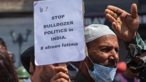 Getty Images SRINAGAR, JAMMU AND KASHMIR, INDIA - 2022/06/17: Kashmiri man holds a placard expressing his opinion during a demonstration. Indian authorities demolished the house of young Muslim activist Afreen Fatima and his father Javeed Mohammad who was arrested in northern Indian state of Uttar Pradesh for allegedly being the "mastermind" behind the recent violent religious protests over blasphemous comments on Prophet Muhammad (PBUH) by India's Hindu nationalist ruling party's suspended spokeswoman Nupur Sharma and expelled leader Naveen Jindal. Protests have been erupting in many Indian cities to condemn the demolition of homes and businesses belonging to Muslims, in what critics call a growing pattern of "bulldozer justice" aimed at punishing activists from the minority group. (Photo by Faisal Bashir/SOPA Images/LightRocket via Getty Images)