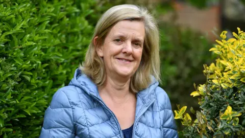 Darren Pepe/Surrey Live A blonde woman in a blue coat standing in between two bushes.