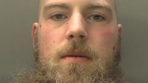 Counter Terrorism Policing Mugshot photo of Alexander Dighton, he is bald with a light brown beard. She has blue eyes and looks straight into the camera lens. 