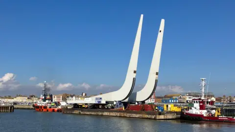 Guy Campbell/BBC One of the white J-beams of the bascule span being shipped to the construction site of the Gull Wing Bridge in March, 2024